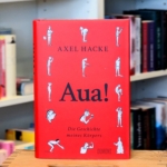 Aua! Das Buch "Aua!" von Axel Hacke vor einem Bücherregal